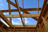 Construction of small wooden frame house. View from below on beams and roof rafters on the background of blue sky.