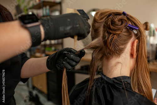 
Close-up of female hands holding the hair rows in professional hairstyles salon. The hairdresser paints or makes keratin to a girl in a professional salon