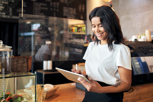 Happy waitress barista using digital tablet at work in cafe, restaurant photo