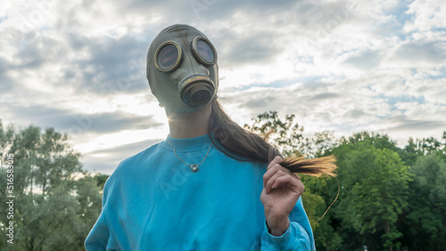 A girl in a gas mask shows her hair. Alienation in the city. Fashion, ecology and loneliness concepts.