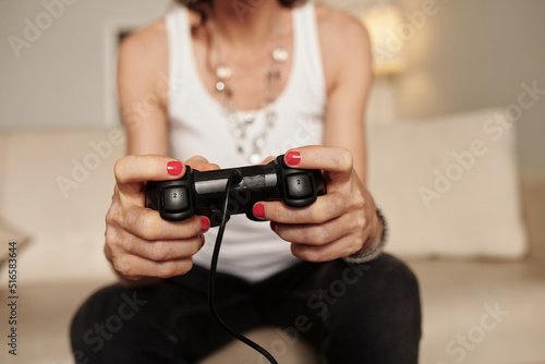 Manicured hands of mature woman playing videogame at home