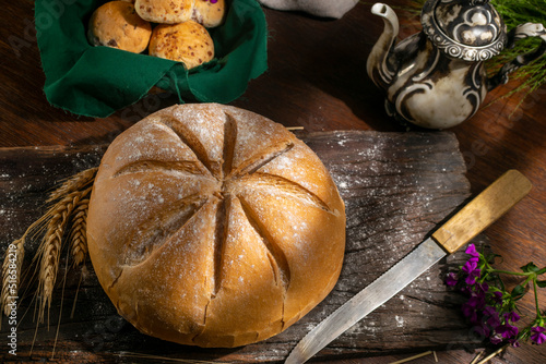 Natural homemade round country bread with smaller loaves with an old teapot decorated with ears of wheat on a country table