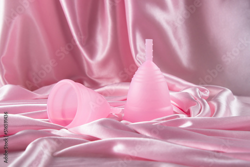 Two menstrual cups of different sizes made of medical silicone, against the background of delicate folds of pink silk and satin photo