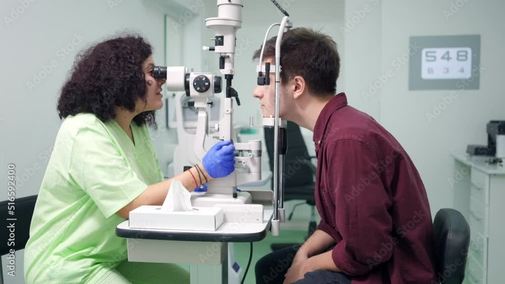 Doctor talking using autorefractor diagnosing patient in hospital indoors. Side view portrait of positive Caucasian woman consulting man in ophthalmological clinic with professional equipment Doctor talking using autorefractor diagnosing patient in hospital indoors. Side view portrait of positive Caucasian woman consulting man in ophthalmological clinic with professional equipment