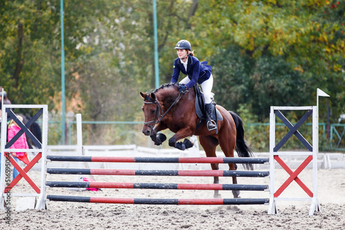 Young female horse rider jumping over the obstacle on equestrian competition
