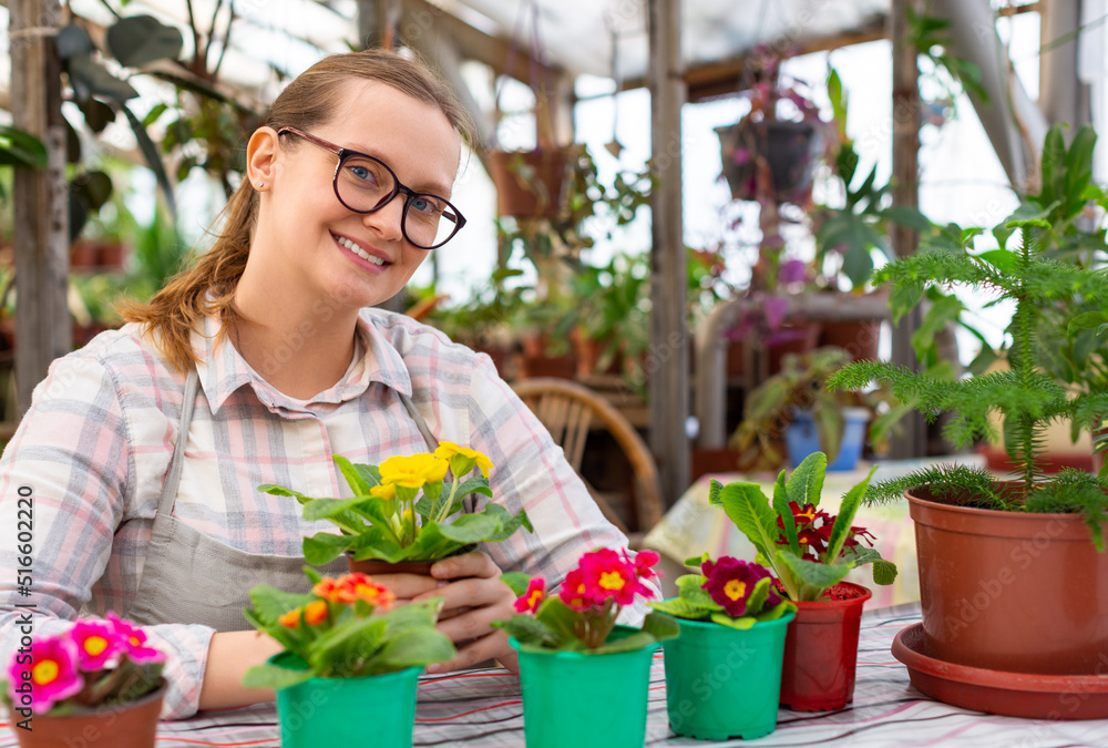 Young woman with a few flowers in a greenhouse - she looking at camera and smiling.