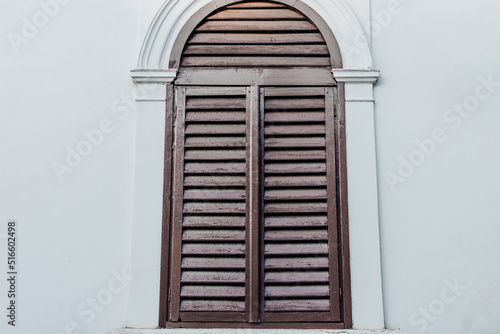 Brown wood window shutters closed on a white exterior home wall