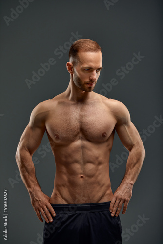 Young male athlete posing. Handsome athletic male power guy. Fitness muscular person. Young athlete showing muscles in the studio  posing shirtless on gray background.