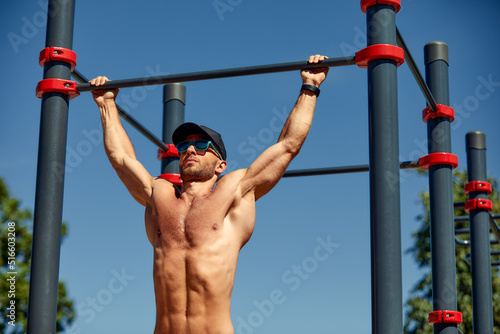 Athletic sportsman trains on the horizontal bars. Training at the open air sprorts ground.