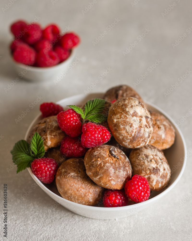 Gingerbread in a white bowl with raspberries close-up in the background a bowl of raspberries in a blur on a light gray concrete background. Vertical arrangement. Gingerbread in a white bowl with raspberries close-up in the background a bowl of raspberries in a blur on a light gray concrete background. Vertical arrangement.