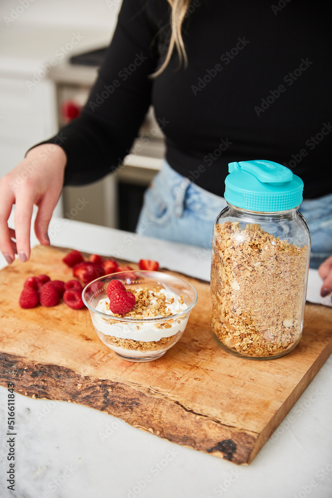 A woman topping yogurt and granola with fruit in a bright modern kitchen