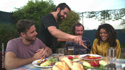 Group of cheerful friends eating barbecue together. BBQ chef serving food to friend. People laughing and smiling