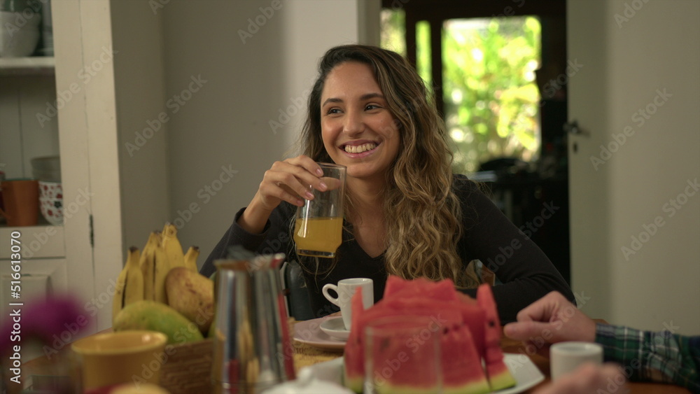 Adult daughter at breakfast table with family talking in the morning holding orange juice in hand Adult daughter at breakfast table with family talking in the morning holding orange juice in hand