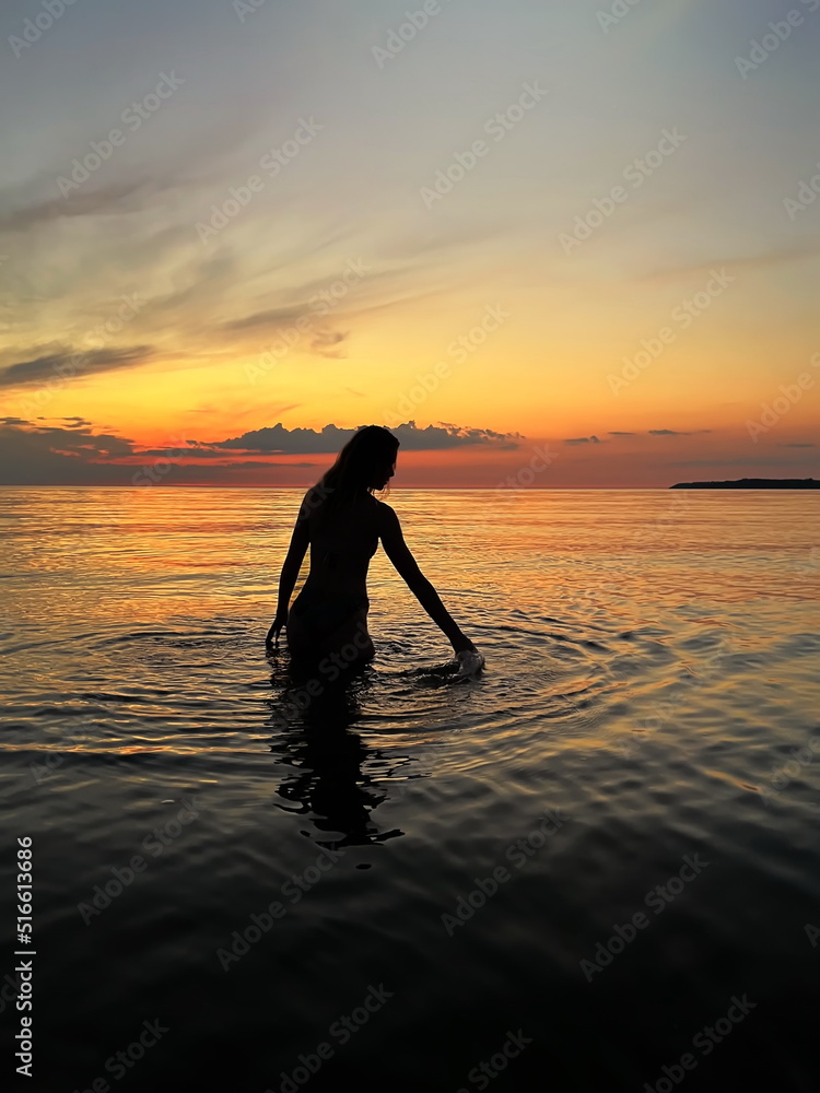 young woman silhouette hand  up and trying touching sun down on  orange sunset at sea summer evening nature landscape 