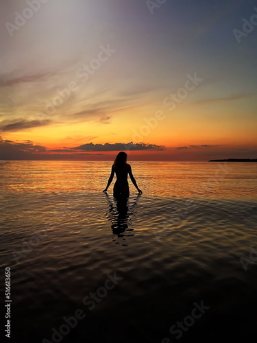 young woman silhouette hand  up and trying touching sun down on  orange sunset at sea summer evening nature landscape  © Aleksandr