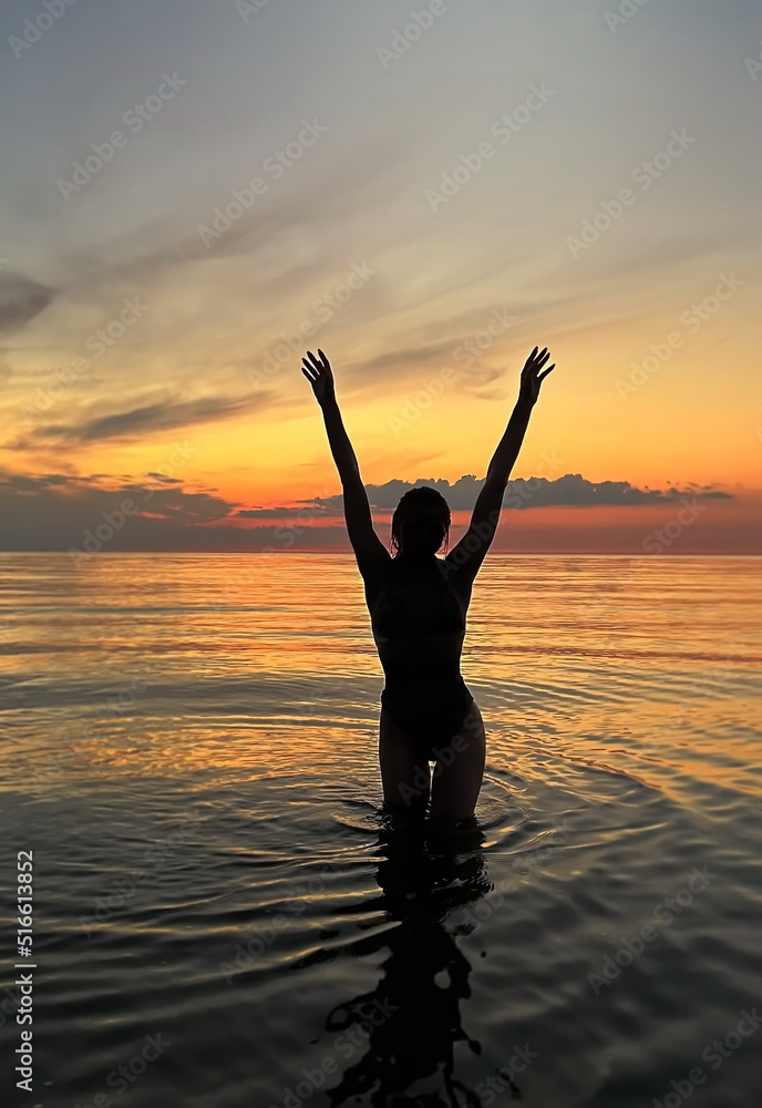 young woman silhouette hand  up and trying touching sun down on  orange sunset at sea summer evening nature landscape 
