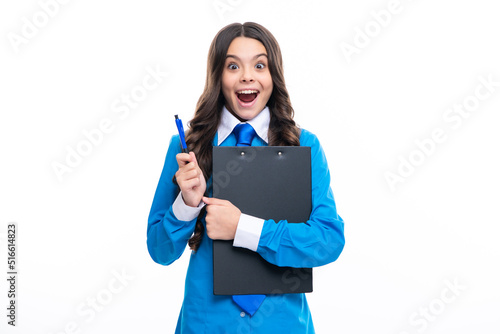 Funny teenager girl in shirt and tie wearing office uniform holding clipboard on white isolated background. Excited face. Amazed expression, cheerful and glad.