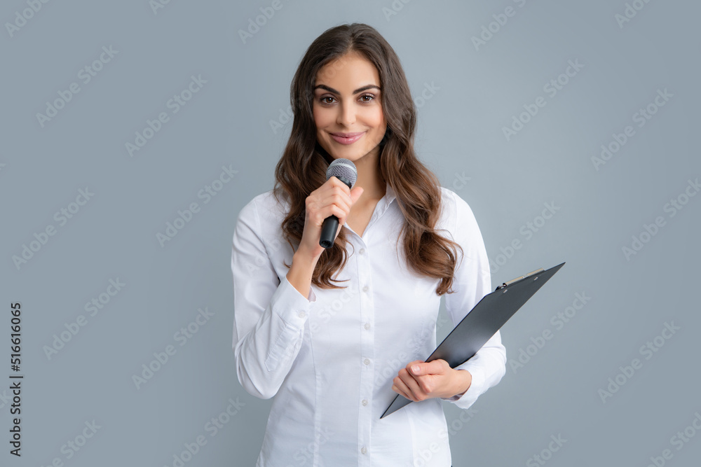 Portrait of young woman journalist in casual shirt holding microphone, asking questions, discussing problems, interviewing. Isolated on gray background. Portrait of young woman journalist in casual shirt holding microphone, asking questions, discussing problems, interviewing. Isolated on gray background.