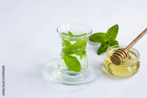 Tea with mint and honey in the glass cup on the white background. Closeup. Copy space.