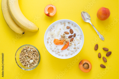 Granola breakfast with milk, fruits and almonds in the white bowl on the yellow background. Top view. Closeup.