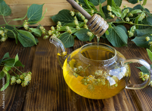 Tea with linden flower and honey in the glass teapotn on the wooden background. Closeup. photo