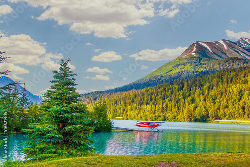 Red sea plane on lake in Moose Pass, Alaska in evening sunshine with mountains in background and surrounded by evergreen trees