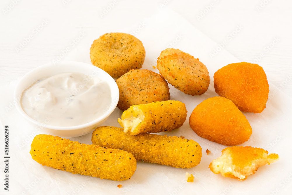 Selection of breaded fried cheese on a white baking paper with white dip. Partially eaten. Selection of breaded fried cheese on a white baking paper with white dip. Partially eaten.