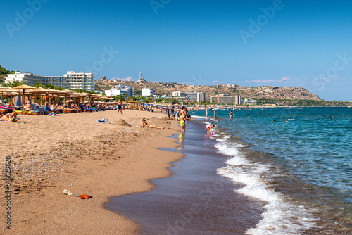 People relaxing on sandy beach at resort Faliraki in Rhodes island, Greece
