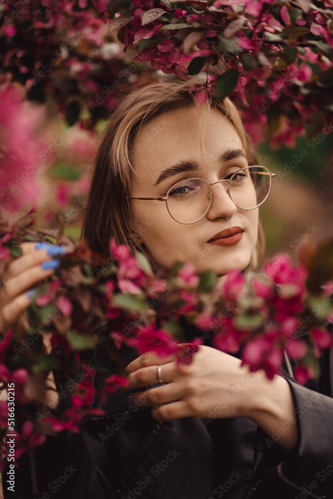 Bright fresh portrait of a young happy blonde girl in black on the backdrop of pink flower tree in autumn as wallpaper, background, magazine cover, poster or advertising design. Bright fresh portrait of a young happy blonde girl in black on the backdrop of pink flower tree in autumn as wallpaper, background, magazine cover, poster or advertising design.