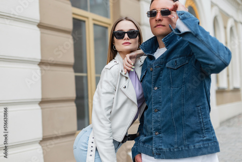 Fashionable beautiful young couple woman and man hipster with vintage sunglasses wearing trendy casual denim with denim jacket and stylish leather jacket are walking in the city