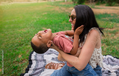 Mother tickling her son, sitting on the grass in a park