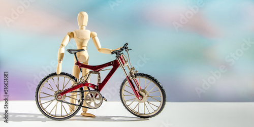 wooden mannequin in form of man near metal model of bicycle. male cyclist stands next to his bike against blurred background of clouds at sunset