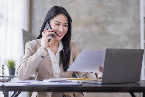 Asian businesswoman working at home with a laptop and talking on smartphone 