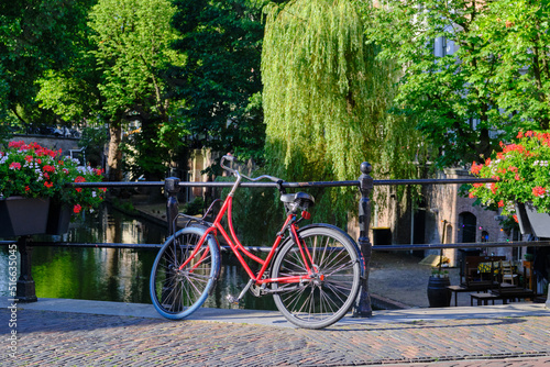 Red bicycle locked and parked on a bridge placed over Oudegracht canal in Utrecht.