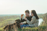 young couple in love on a picnic in nature with their pet, a big red dog. Young people eating hamburgers outdoors