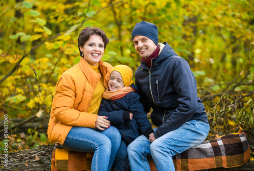 Mother, father and little son sit on a plaid on a log in the autumn park and spend time together © ribalka yuli
