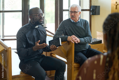 Fototapeta Confident pastor in black shirt with clerical collar explaining verses from Bibl