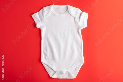 Flat lay mockup of a white baby bodysuit on a red background, for girls. Layout for the design and placement of logos, prints, advertising.