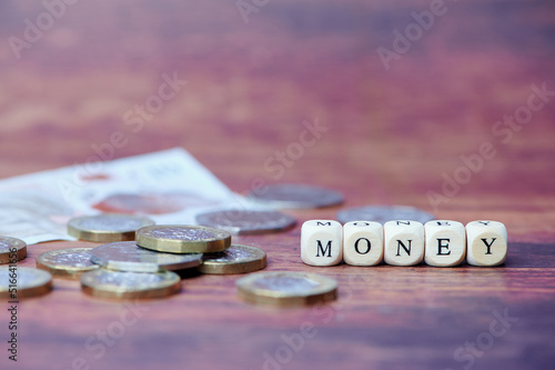 wooden cubes with the English word money, beside are some British pound coins, copy space on wooden background