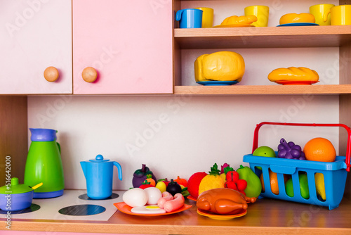 Multicolored toy dishes, vegetables and fruits made of plastic stand on a children toy kitchen.