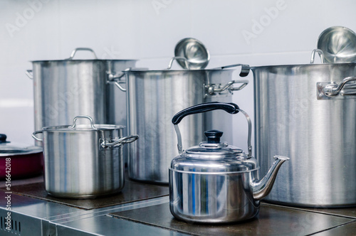 Metal kettle, pots, scoops stand on an electric stove in a professional kitchen