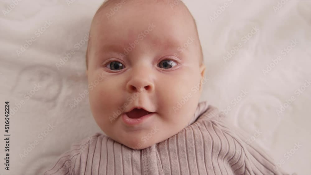 Cute funny little newborn baby smiling, lying at the back in the child crib looking around. Portrait playful child. Close up. Slow motion Cute funny little newborn baby smiling, lying at the back in the child crib looking around. Portrait playful child. Close up. Slow motion