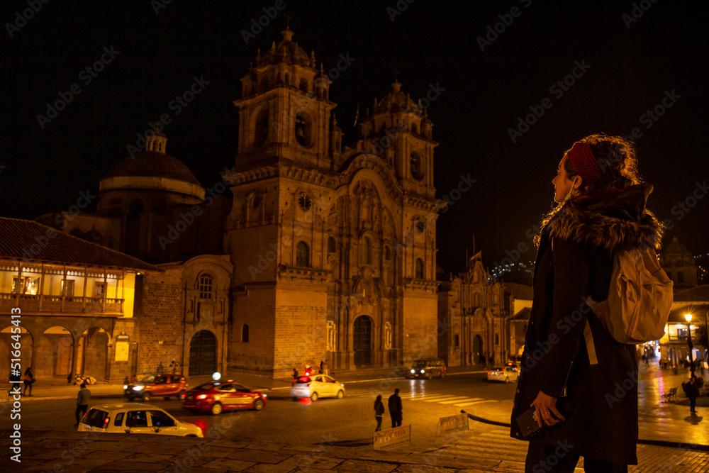 Tourist woman looking at church at night in the main square in Cusco, Peru