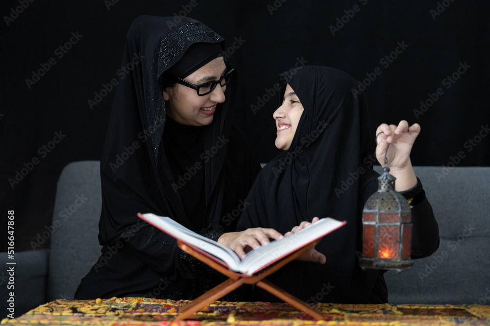 muslim mother with her daughter reading a holy book Quran and holding lamp on black background muslim mother with her daughter reading a holy book Quran and holding lamp on black background