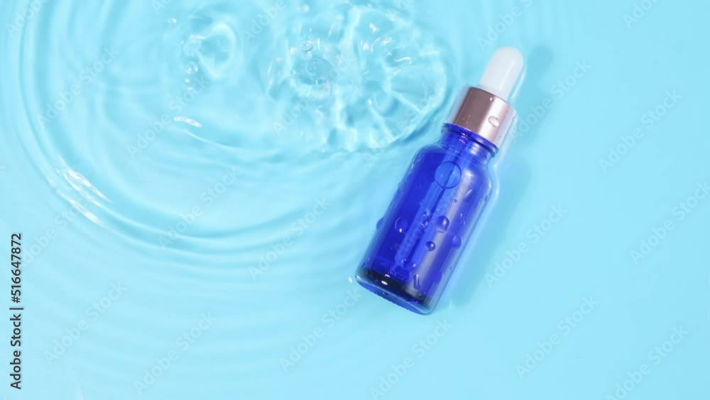 advertising slow motion, Glass cosmetic bottle with pipette lies on the surface of the water. Top view of drop falls into water and diverging circles of water on blue background. packaging for design advertising slow motion, Glass cosmetic bottle with pipette lies on the surface of the water. Top view of drop falls into water and diverging circles of water on blue background. packaging for design