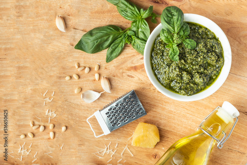 Ingredients for pesto sauce in the white bowl. Green basil leaves, Parmesan cheese and pine nuts on the wooden background. Flat lay. Overhead view