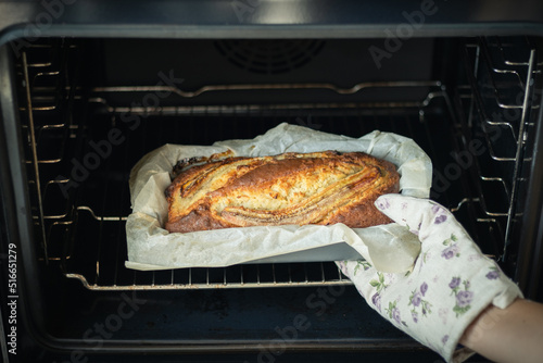 Woman wearing potholder taking fresh banana bread out of the oven. Close up of hot homemade pastry