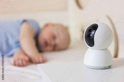 Cute little baby boy sleeping on bed at home with baby monitor camera.