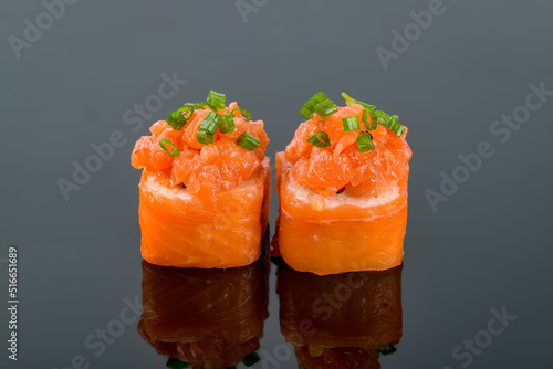 salmon roll with green onion on black background with reflection