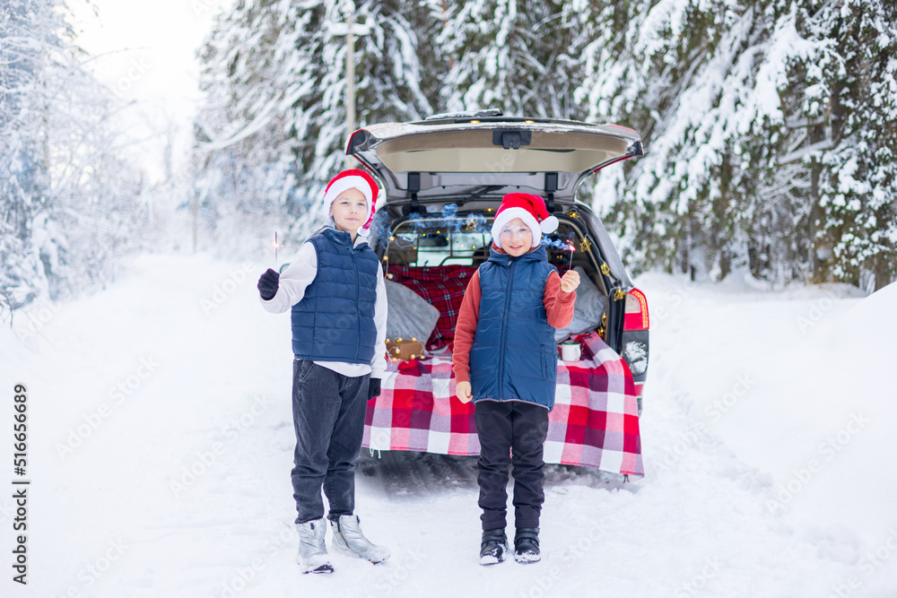 two children friends boys in Santa hats traveling and having fun in trunk car in snow winter forest with sparklers, talking and getting ready to celebrate Christmas or New year together